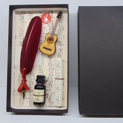 Conjunto de pena vermelha, mini guitarra, pote de tinta e rolo de papel com pauta musical numa caixa preta
