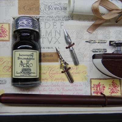 Frasco de tinta preta, bicos metálicos, suporte de estilete e objeto marrom sobre papel decorativo