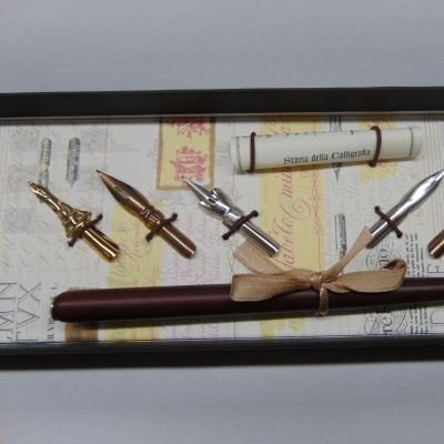 Conjunto de caligrafia numa caixa preta com várias pontas metálicas e caneta de madeira castanha.