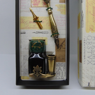 Conjunto de escrita vintage com tinteiro, caneta de pena dourada e suporte metálico em caixa decorada.