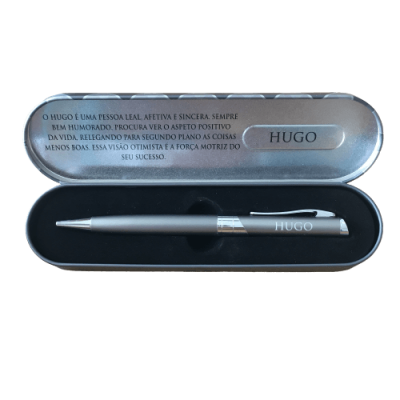 Estojo metálico com caneta prateada e texto sobre HUGO no interior da tampa