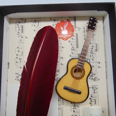 pena vermelha grande, miniatura de guitarra clássica, pauta musical e etiqueta La Kuarteria