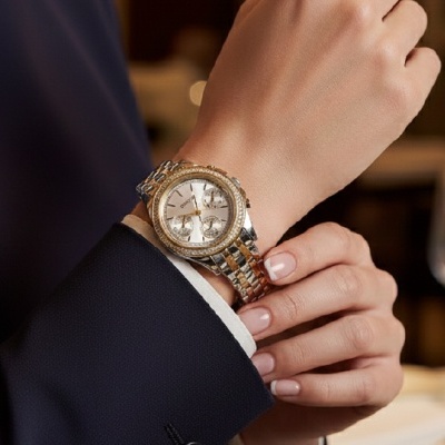 Relógio de pulso dourado e prateado num pulso feminino com manicure nude
