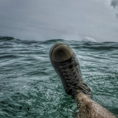 Sapatilha preta amarrada num pé submerso na água do mar sob céu nublado