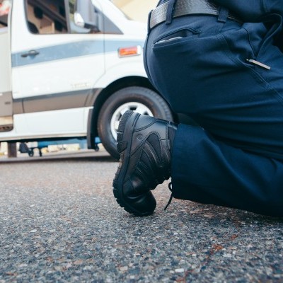 Botas pretas robustas com calças azuis escuras ajoelhadas em asfalto com carrinha branca ao fundo