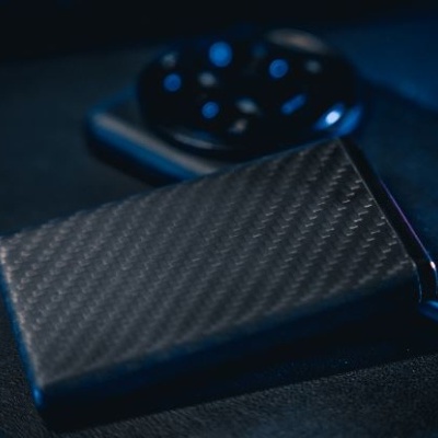 Carteira de padrão fibra de carbono preto junto a dispositivo cinza com mostrador preto e botões azuis