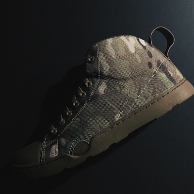 Bota militar camuflada em tons terra sobre fundo preto