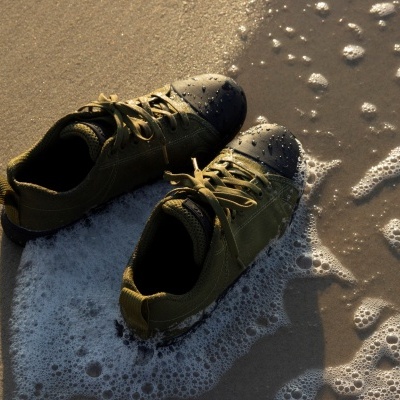 Sapatos desportivos verdes na areia da praia com espuma de água do mar