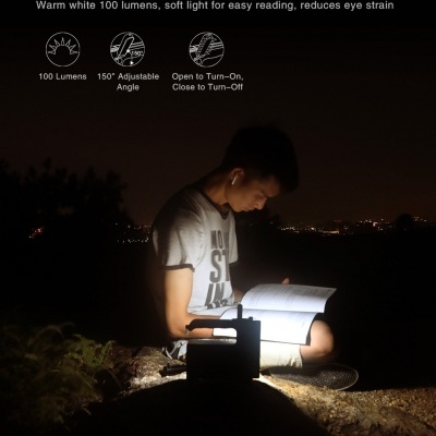 Lâmpada de mesa dobrável a iluminar jovem a ler livro ao ar livre à noite