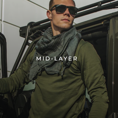 Homem com camisola verde e óculos escuros ao lado de jipe preto com texto MID-LAYER