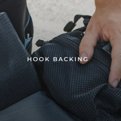 Mãos sobre mochila preta com detalhe em malha e texto 'HOOK BACKING'