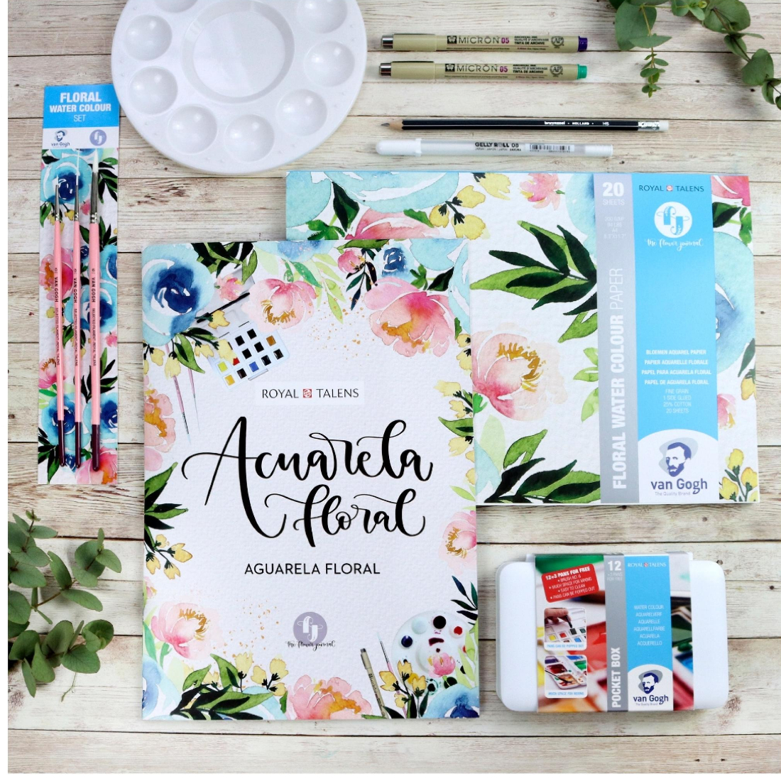 Conjunto de materiais para aguarela floral com pincéis, paleta e blocos de papel decorados com flores.