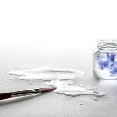 Pincel molhado com tinta branca e frasco de tinta azul sobre superfície clara.