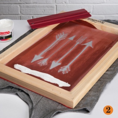 Ecrã de serigrafia com desenho de setas brancas e tinta branca numa superfície de tecido cinzento