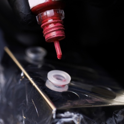 Frasco com tinta vermelha e gota saindo numa superfície metálica reflexiva