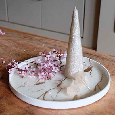 Prato redondo branco com vela cónica bege com brilho e flores rosas sobre mesa de madeira