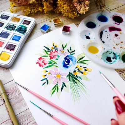 Mesa com material de pintura, pincéis, paleta e desenho floral em aguarela