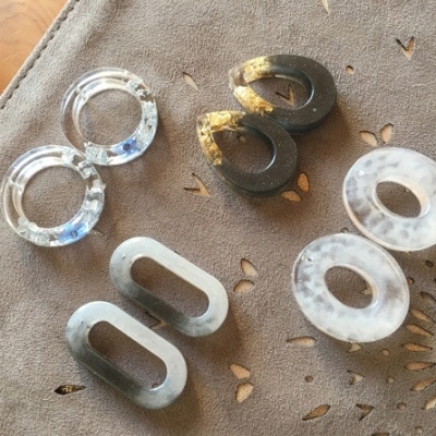 Joias artesanais em resina de várias formas e cores sobre pano bege com padrão floral