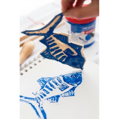 Carimbo de madeira em forma de peixe pintado de azul ao lado da impressão correspondente num papel branco.