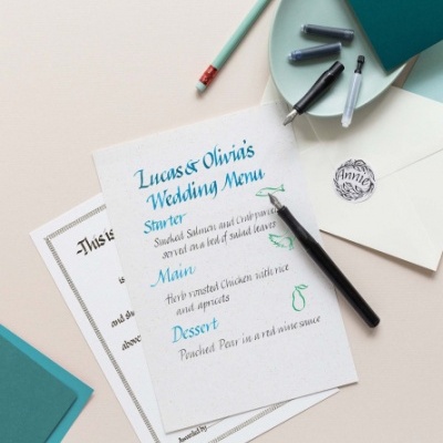 Menu de casamento, caneta, lápis e envelope sobre superfície clara e azul