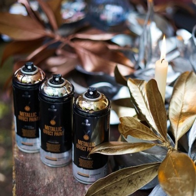 Três latas de spray metálico para pintura junto a folhas douradas e vela acesa