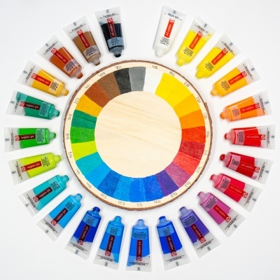 Tubos de tinta acrílica coloridos dispostos em círculo em torno de uma roda de cor em madeira