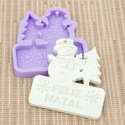 Molde de silicone lilás e objeto decorativo branco com boneco de neve, árvore de Natal e texto FELIZ NATAL