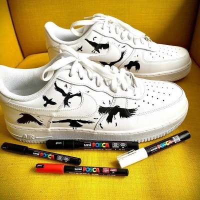 Ténis brancos com desenhos de pássaros pretos e marcadores Posca ao lado