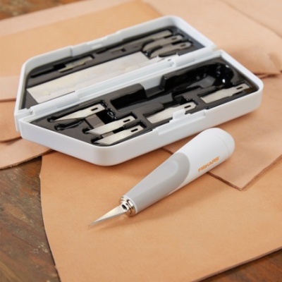 Kit de lâminas cortantes com cabo branco sobre folhas de couro castanho