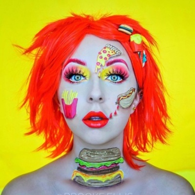 Pessoa com maquilhagem vibrante e cabelo laranja com pinturas de comida rápida no rosto