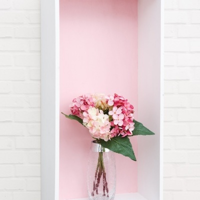 Vaso de vidro com flores artificiais em prateleira branca com fundo rosa