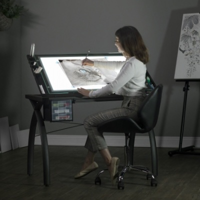 Mulher a desenhar um gato numa mesa de desenho iluminada, cadeira preta e ambiente de escritório cinzento