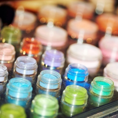 Frascos pequenos com pós coloridos em tons variados numa superfície reflexiva.