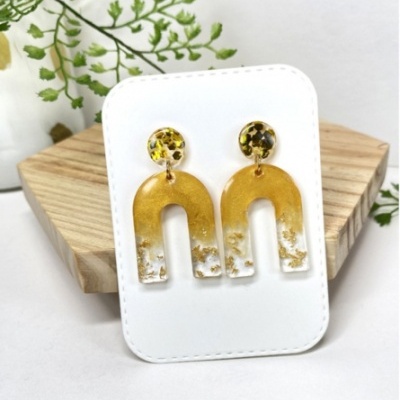 Brincos de resina amarelos com padrão preto e branco em cartão branco sobre madeira