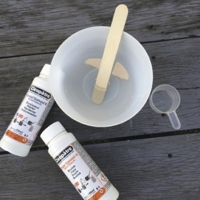 Dois frascos Sikaplatre, copo branco com misturador de madeira e medidor plástico sobre madeira escura