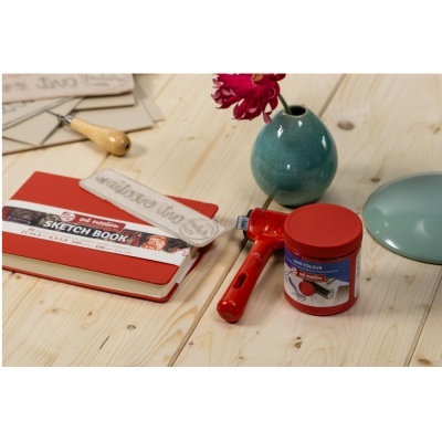 Mesa de madeira com livro de esboços vermelho, rolo vermelho, tinta vermelha e vaso azul com flor