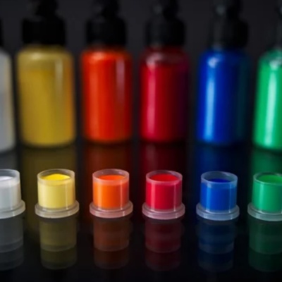 Tintas acrílicas coloridas em frascos plásticos com amostras em pequenos recipientes transparentes.