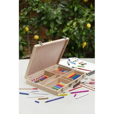Estojo de madeira aberto com material de desenho colorido sobre mesa branca, árvore com limões ao fundo