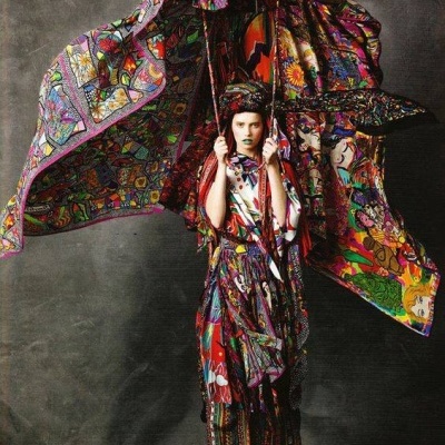 Roupa feminina colorida com padrão abstrato, capa grande, saia e blusa, sapatos laranja.