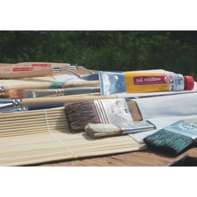 Pincéis de pintura, tubos de tinta e rolo de tecido sobre uma superfície de madeira com fundo verde