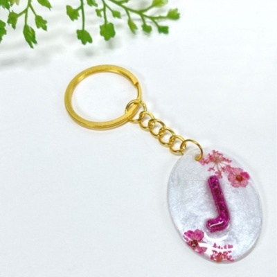 Porta-chaves oval transparente com letra J em glitter roxo e flores rosas, com argola dourada