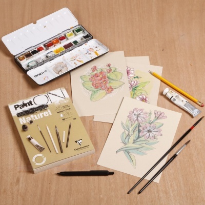 Conjunto de pintura com aguarelas, caderno, desenhos florais e materiais de pintura sobre madeira