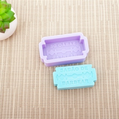 Dois moldes de silicone lilás e azul para sabonete com texto 'SABÃO DE BARBEAR' junto a planta suculenta