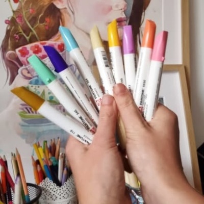 Mãos segurando marcadores coloridos com quadro de ilustração ao fundo