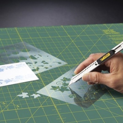 Tapete de corte verde com régua plástica e estilete a cortar folhas brancas