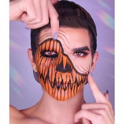 Homem com maquilhagem de caveira laranja e preta com boné e unhas compridas