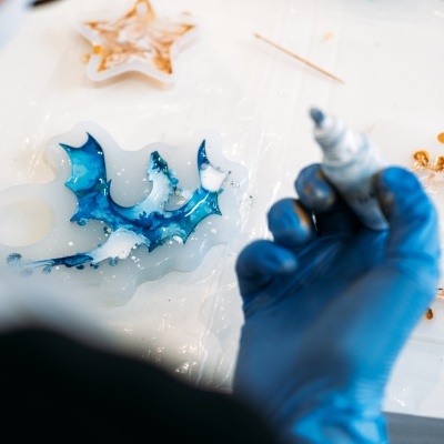 Mão com luva azul pintando molde de silicone em forma de dragão com tinta azul