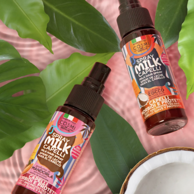 Frascos de spray capilar com rótulo colorido sobre folhas verdes e tecido rosa com metade de coco