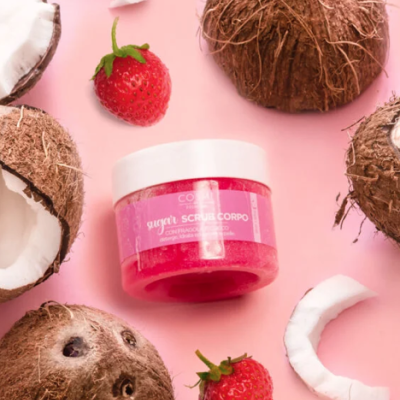 Frascos de esfoliante corporal com coco e morangos em fundo rosa