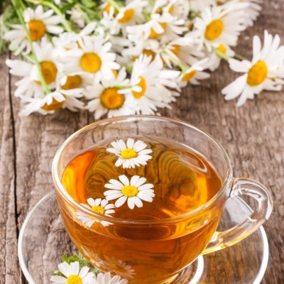 Chávena de chá de camomila com flores flutuantes e flores frescas em madeira